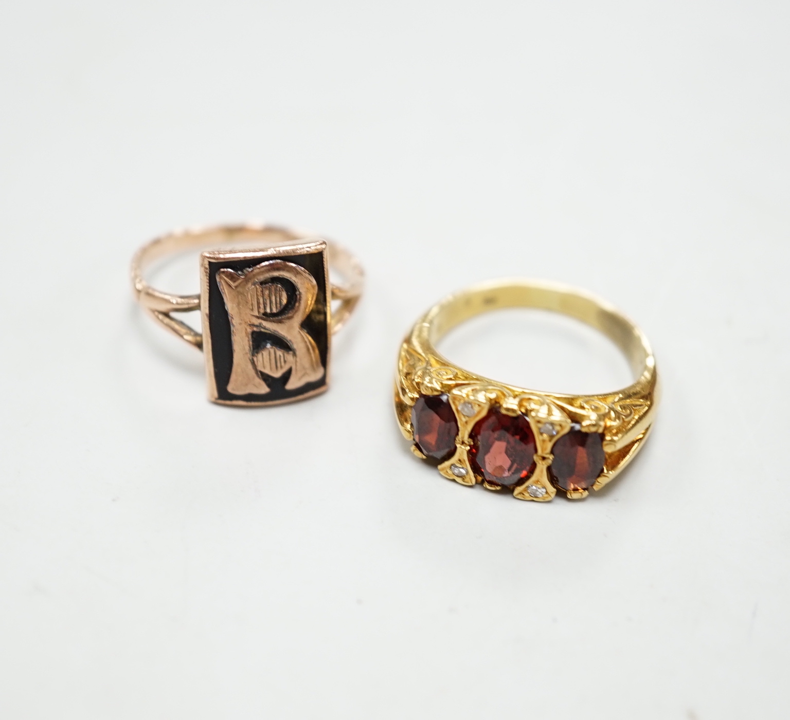 A yellow metal and three stone garnet set ring, with diamond chip spacers and a 9ct and black enamel set initial ring, gross weight 10.1 grams.